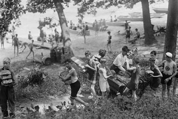 Group of Boys carry loaves of bread from wagons near beach front in woods. - Art Print